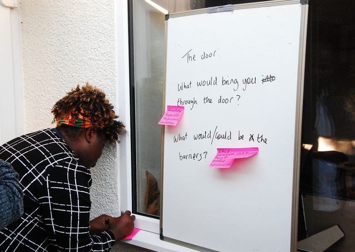 A guest adding a note to the whiteboard asking what would bring people through the door, and what the barriers might be.